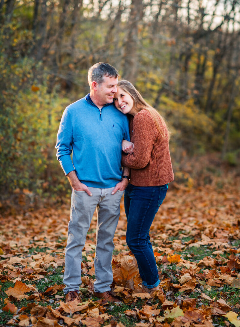 A couple standing close together in a fall setting, sharing a warm smile by Leslie Q Photography