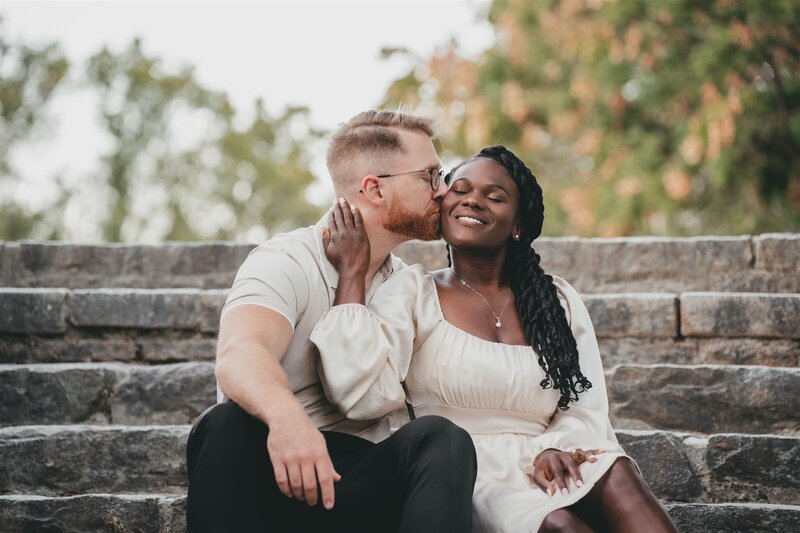 man kissing woman on the cheek while they sit on stone steps