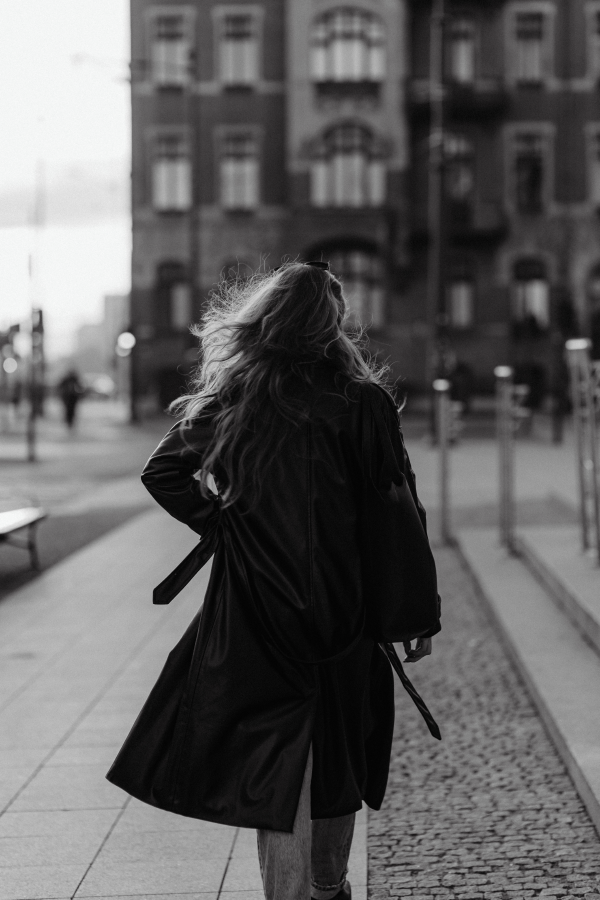 Black and white image of girl in coat walking through town heading twoards brick building | BrandBy Design