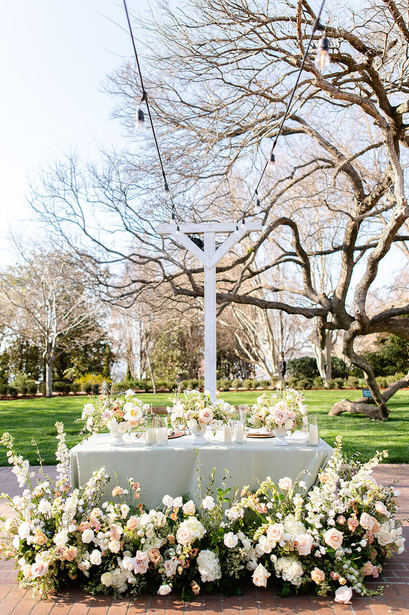 Atlanta wedding planner, Tyler Albritton's  sweetheart table set up from her wedding at the Dallas Arboretum & Botanical Gardens. It features a pastel green tablecloth, with an abundance of florals on top of the table, and many pastel florals around the front in shades of pink, cream, and green