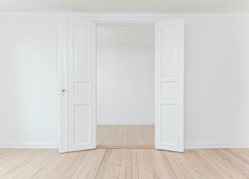 Two white french doors opening up to an empty room with hardwood floor