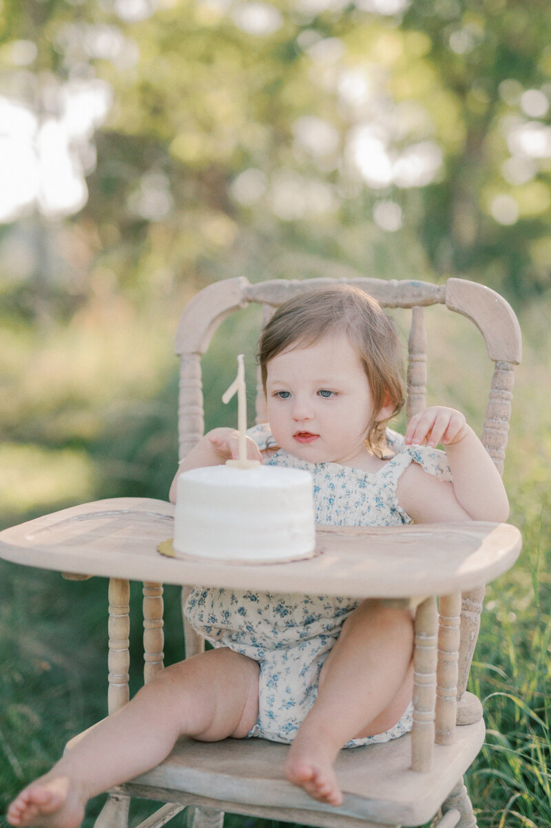 little girls first birthday with a small cake in a vintage high chair