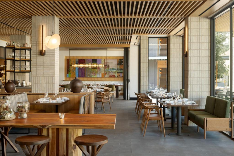 A black-and-white close-up of a place setting with a floral-illustrated menu, layered plates, and a glowing candle.
