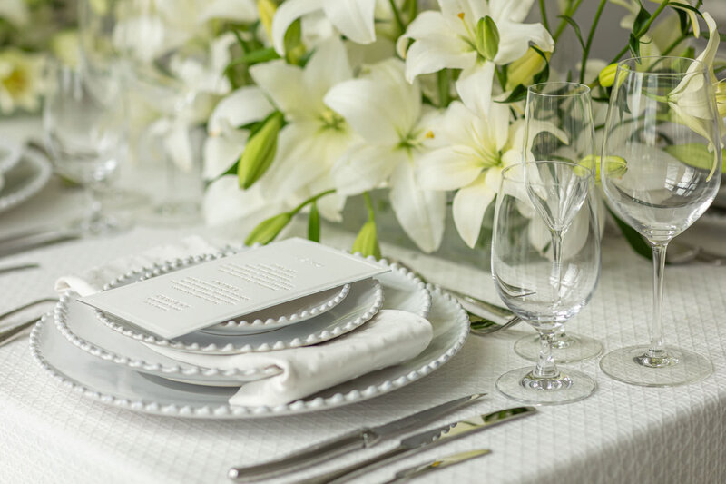 White on white wedding reception table featuring pearl rimmed dishware and hammered flatware