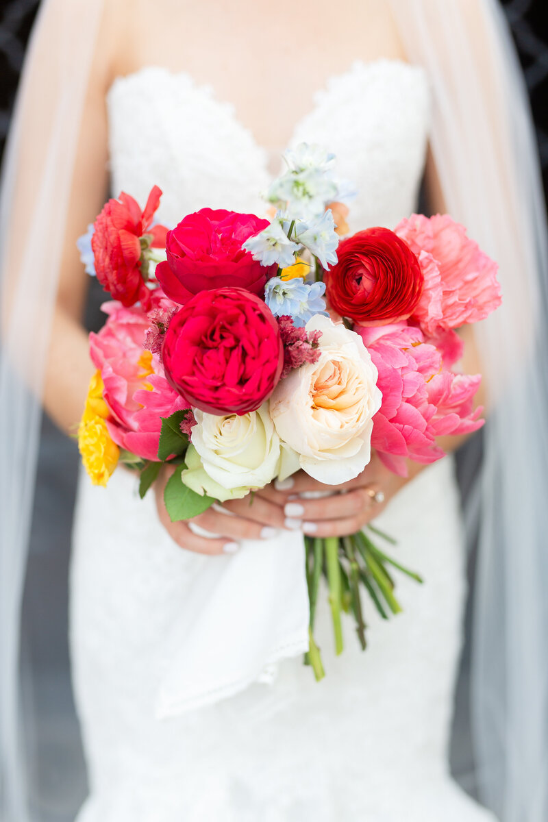 Close up of bride holding a bright pink and white flower bouquet in front of her dress