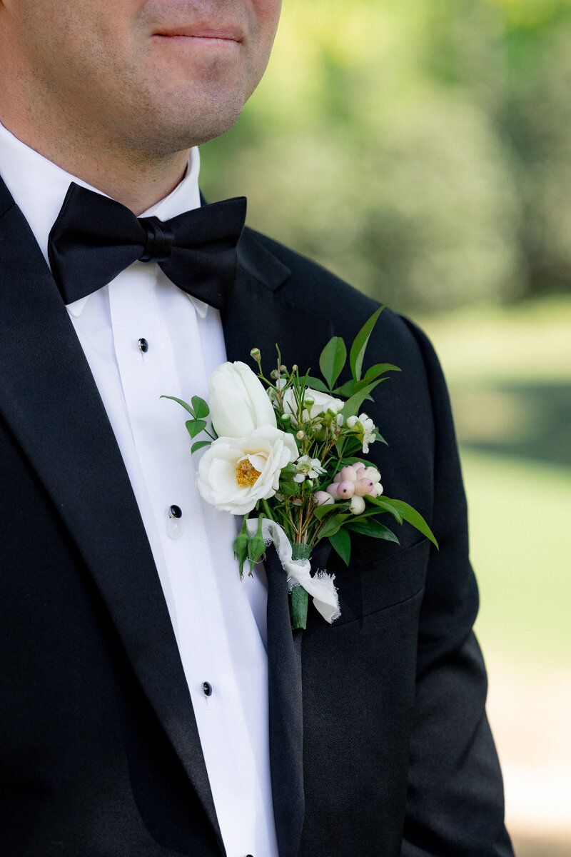 Groom in tux showing his boutonniere up close