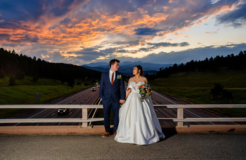 Bride and groom standing on the wooden bridge at Christies of Genesee with sunset mountain views in Golden, Colorado.