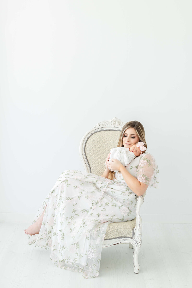 Woman holding baby sitting in a chair during newborn photography session in Dothan alabama photography studio