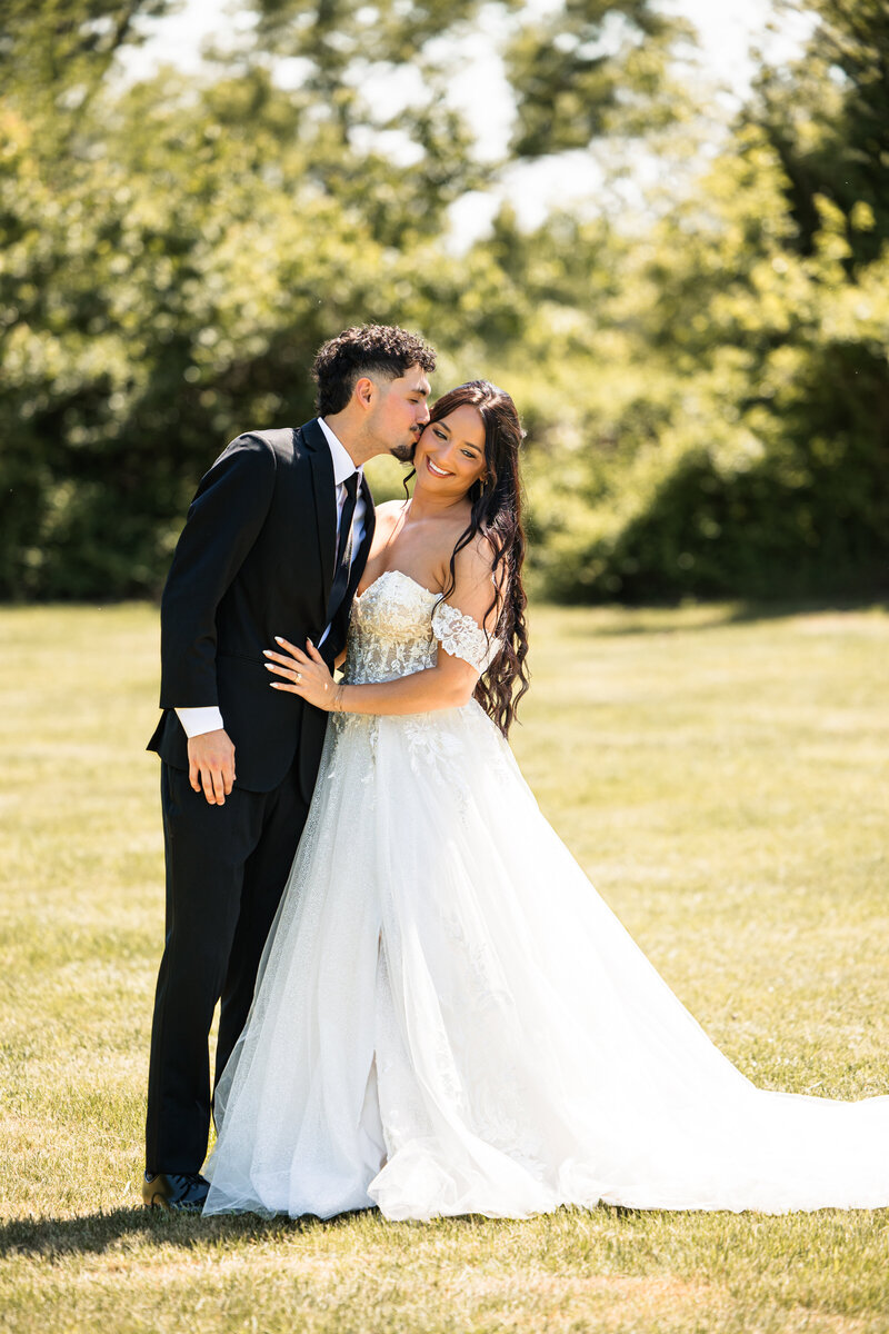 Bride smiling as groom kisses her cheek during joyful wedding portraits in Wichita Kansas