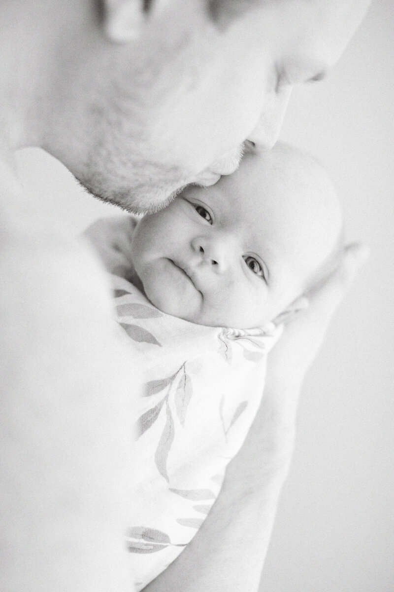 black and white of dad kissing swaddled baby by Chicago Newborn Photographer