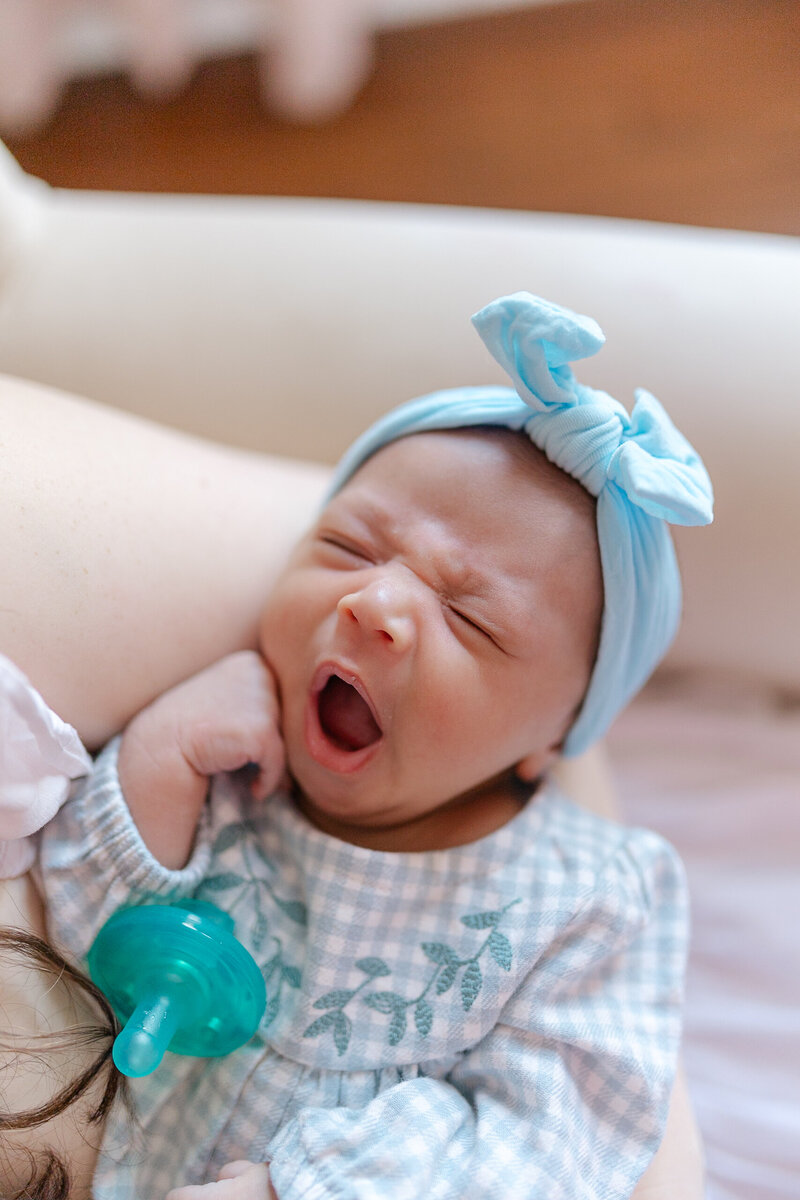 Newborn baby yawning while being held in mother's arms.