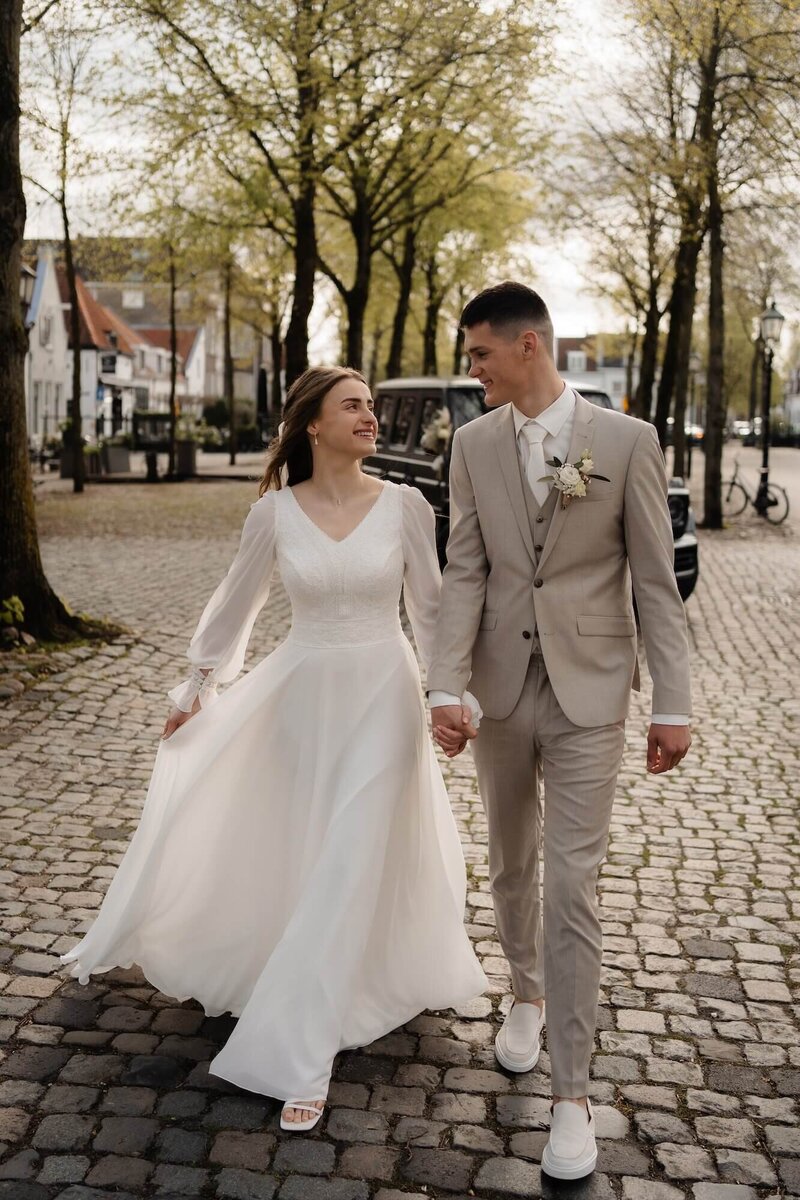 Een bruid en bruidegom wandelen samen over een kasseistraat, vastgelegd door trouwfotograaf Julia de Groot