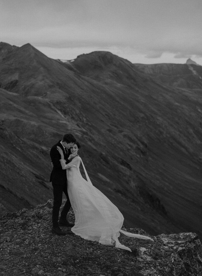 Groom kisses bride on the edge of a cliff in the San Juan Mountains