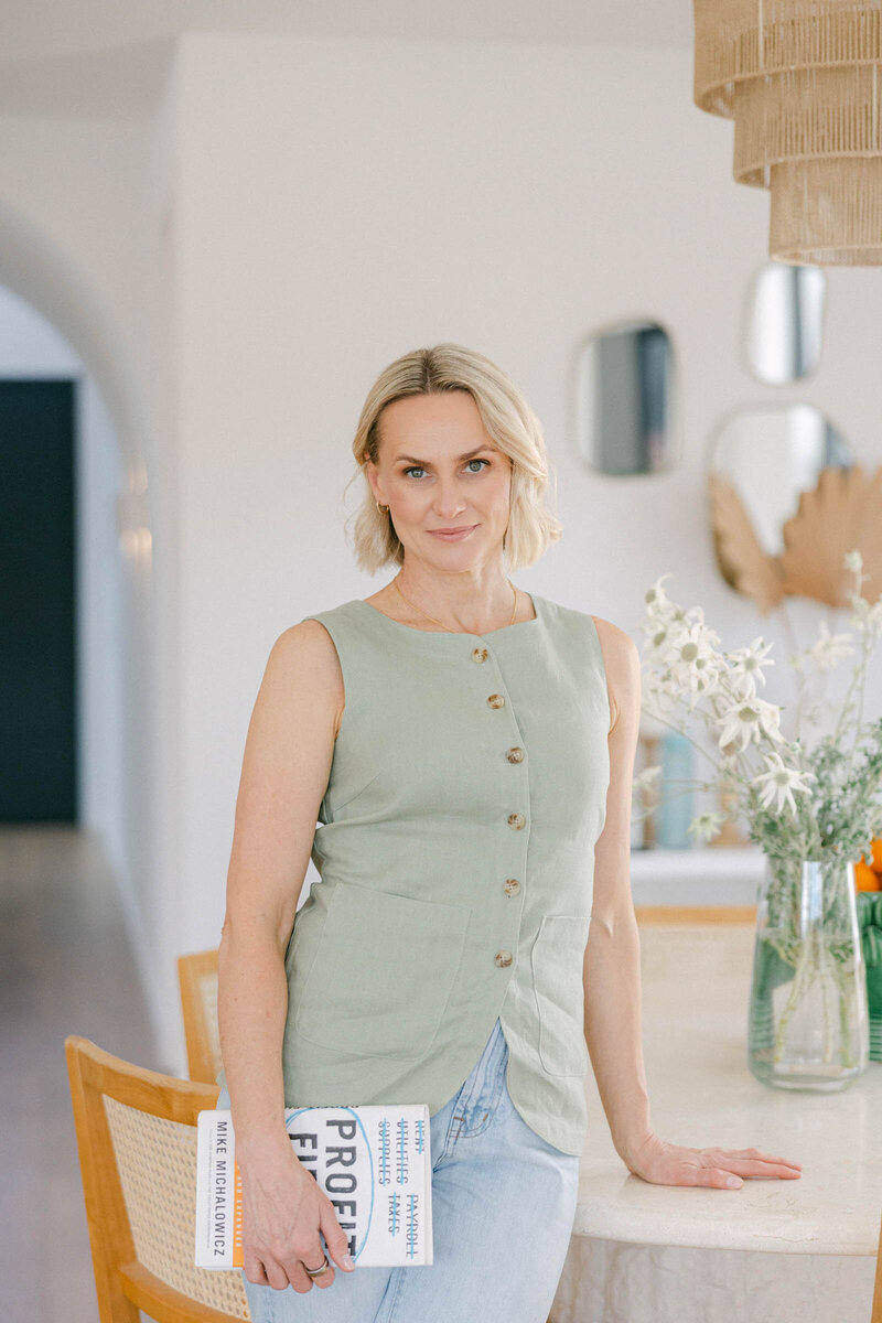 Zelda Green, entrepreneur and money and mindset educator, smiling at camera while working on her laptop on her business resources in her beautiful home
