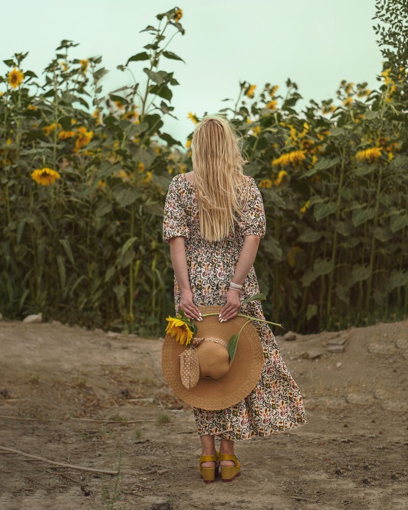 Girl standing in front of sunflower field with har
