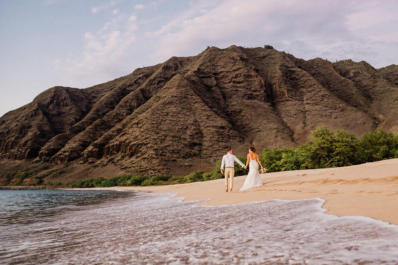 bride and groom holding hands walking along the beach