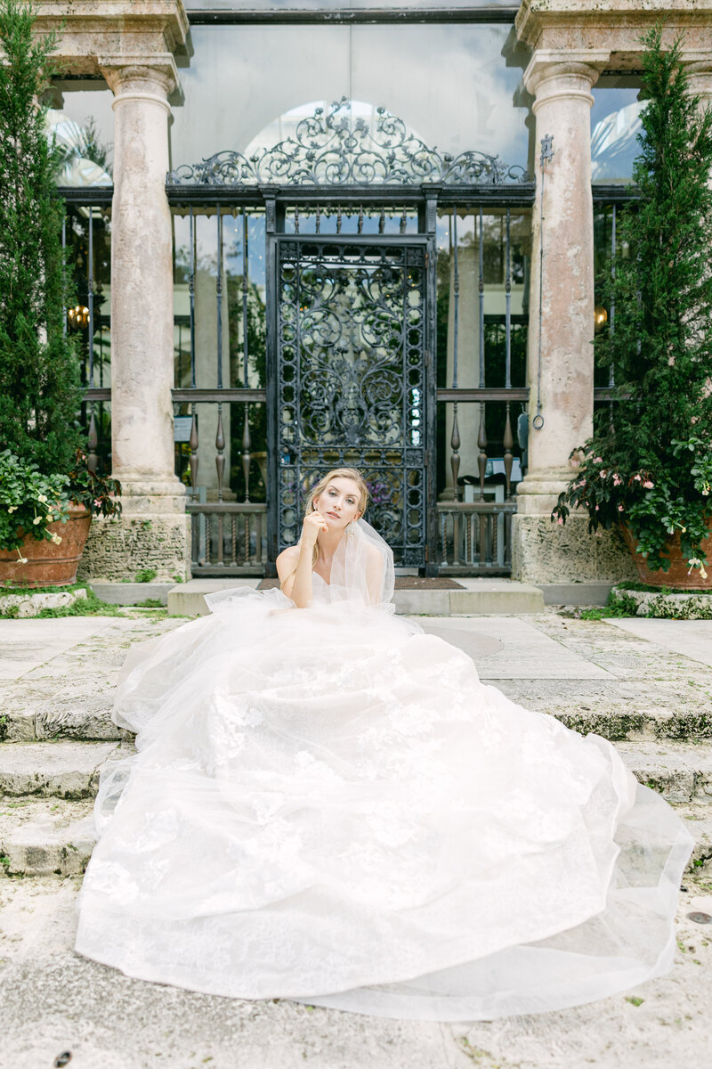 Elegant bride in a voluminous lace wedding gown at the historic Vizcaya Museum in Miami. A luxury editorial wedding portrait with European-inspired architecture.
