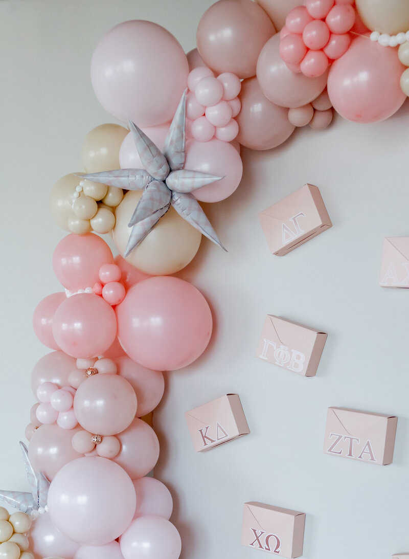 Balloon garland on white wall with pink envelopes and disco balls.