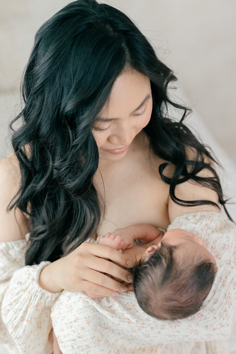 A mom holding her newborn baby while gazing down at her in all white studio by New Jersey baby photographer