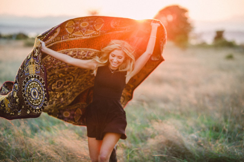 High school senior female  twirling with patterned shawl at sunset in field at Discovery Park in Seattle.
