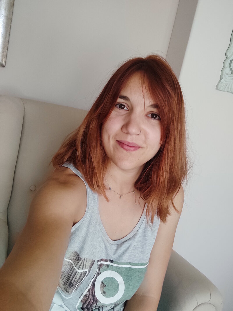 Danae Karachaliou at Writing Pajamas shown sitting on an armchair smiling at the camera 