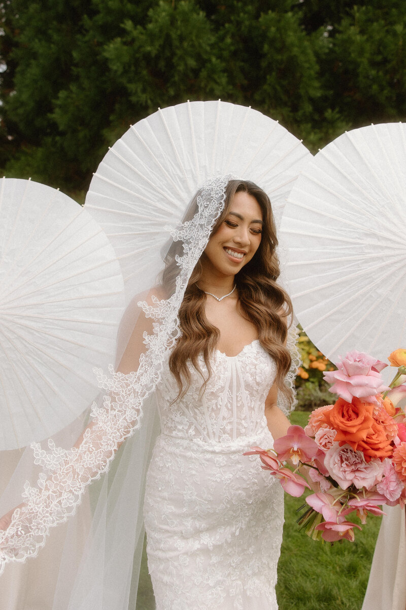 Bride stands with her bridesmaids, long cathedral veil holding a colourful pink bouquet 