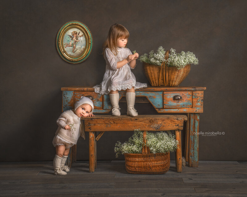 Two girls with babies breath flowers on antique desk. Vintage style fine art photos. Grande prairie photographer. Grande Prairie portrait studio. Photography workshops.