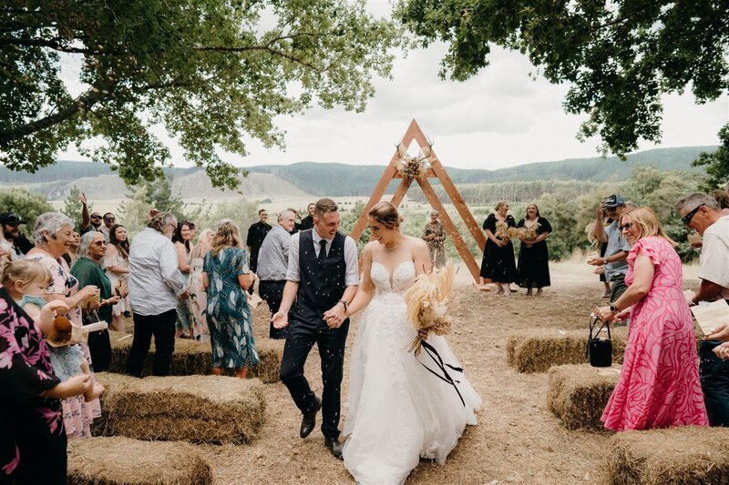 A bride and groom smile at each other as confetti is thrown as they exit their wedding ceremony and are photographed by Tashina Narelle