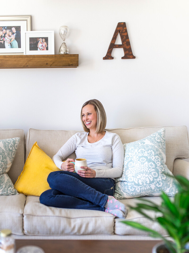 A headshot of Amanda Miller on the sofa drinking a cup of coffee.