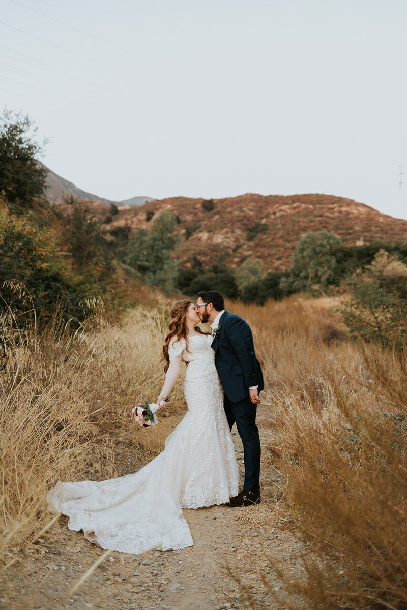 Bride and groom kissing in a field below a mountain in Rancho Cucamonga California.