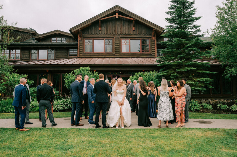 A bride stands amongst family and friends, lifting up her dress and grinning at the camera.