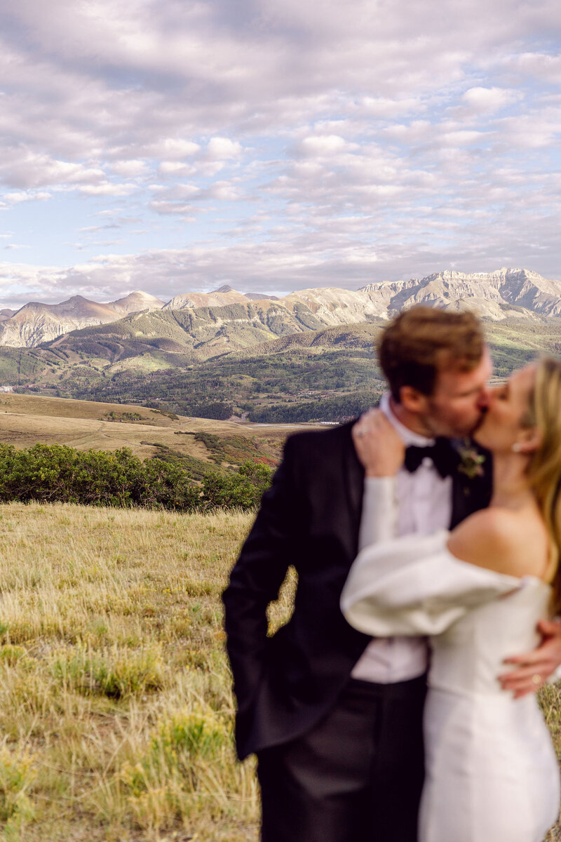 couple kissing in front of a beautiful landscape of mountains, cloudy sky, green grass