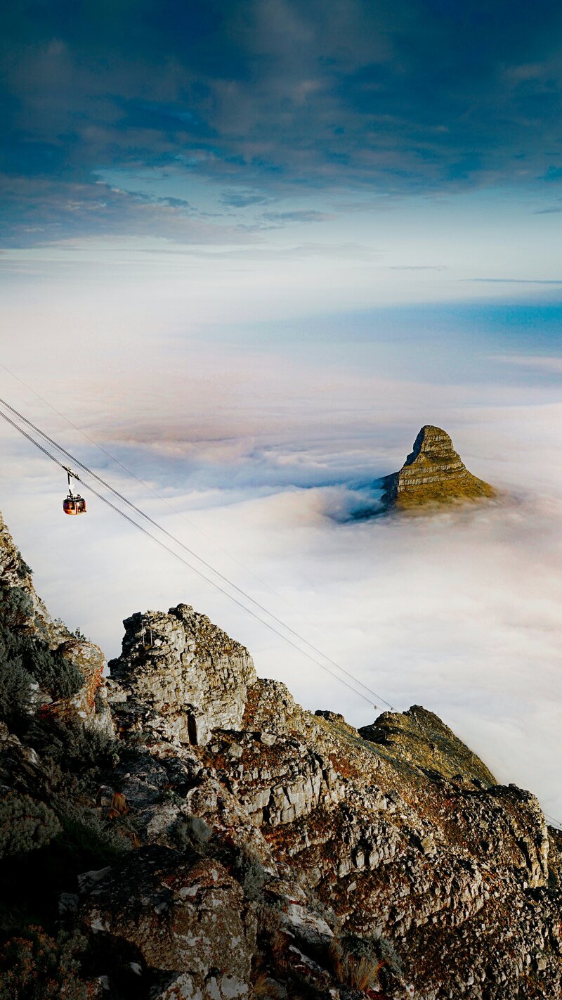 Table Mountain in Cape Town, partially covered by clouds, with a red cable car ascending the side.