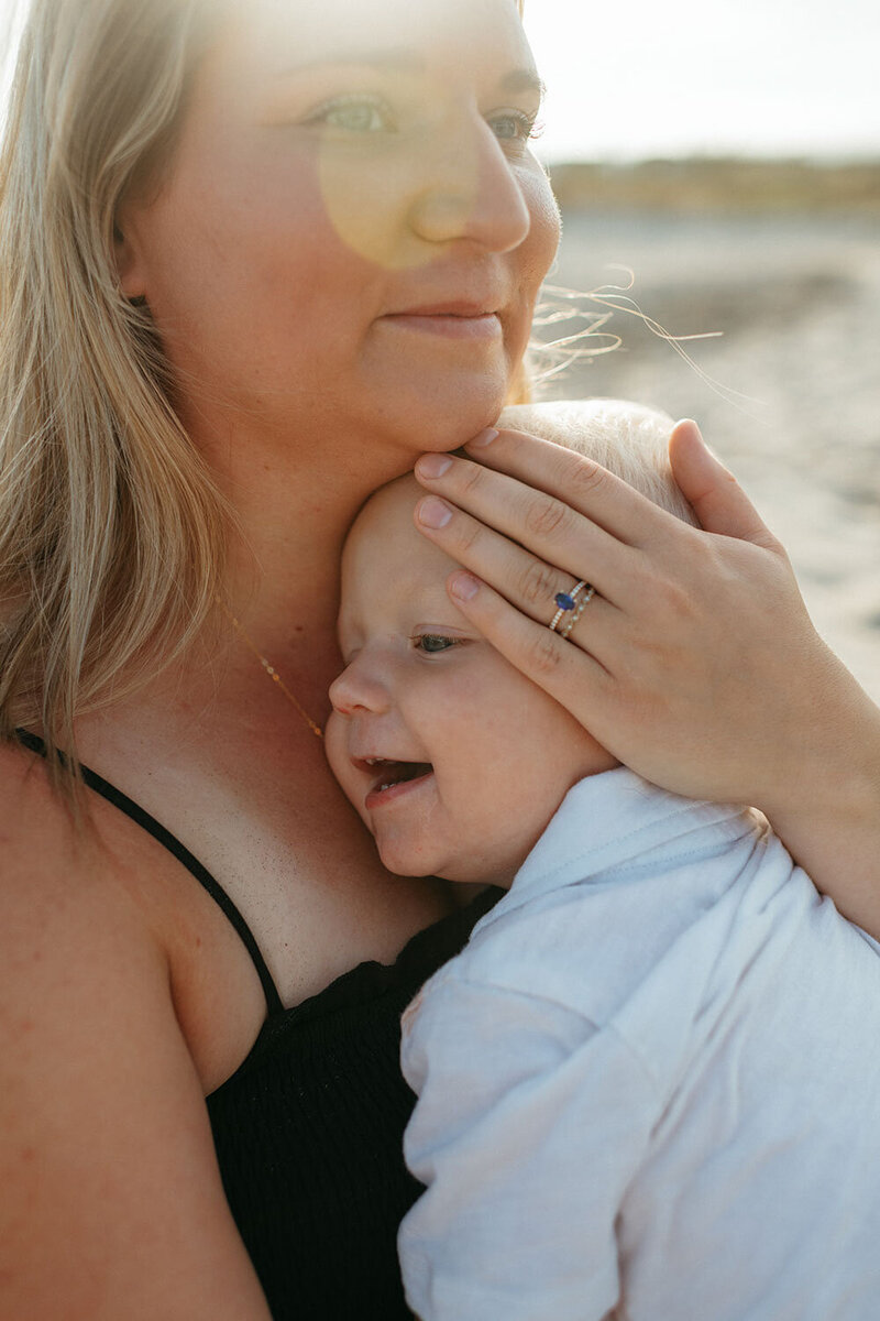 Molly, a San Diego Photographer  holding her baby close, gently resting her hand on the baby’s head