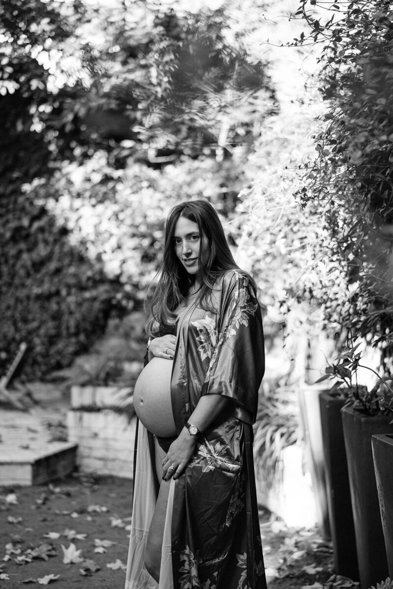 Pregnant mother to be standing in silk robe in her London garden