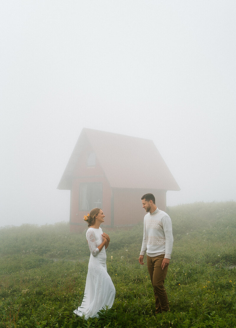 Bride and groom looking at each other lovingly with a red cabin behind them