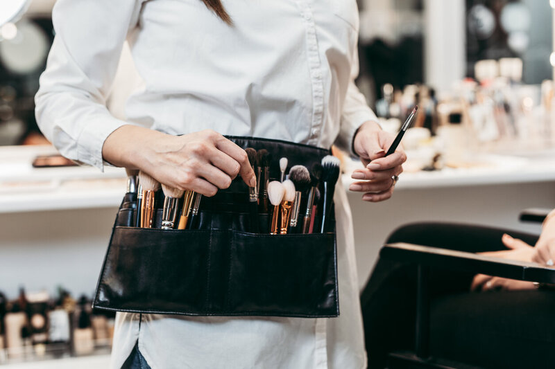 Make up artist helping client holding makeup brush and mirrors in the background