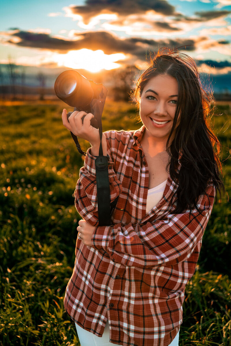 Emily Belanger holding a camera in front of a sunset
