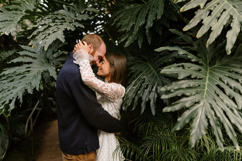  A couple shares a warm embrace in a beautiful tropical garden filled with lush plants and bright blossoms.