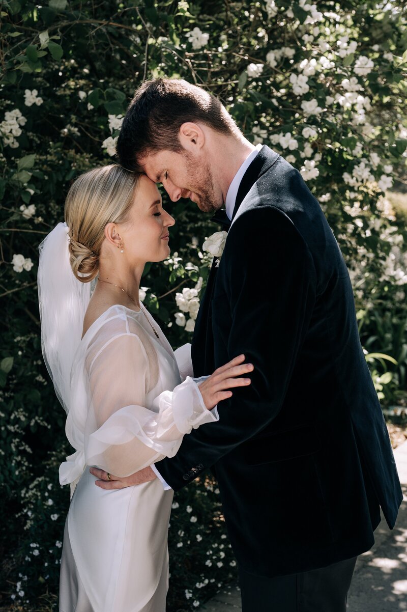 bride in kenny and harlow dress with chignon and groom in tuxedo in christchurch garden on their wedding day