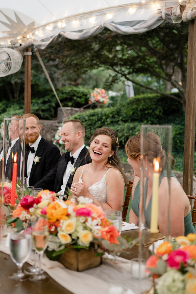a bride laughs at a dinner table surrounded by colorful floral arrangements