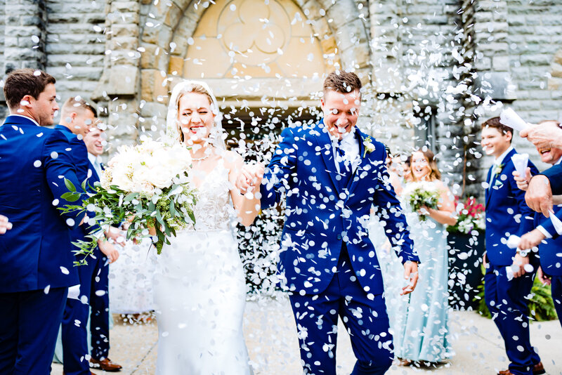 a laughing wedding couple walking through a cloud of flower petals after the ceremony in Toledo Country Club