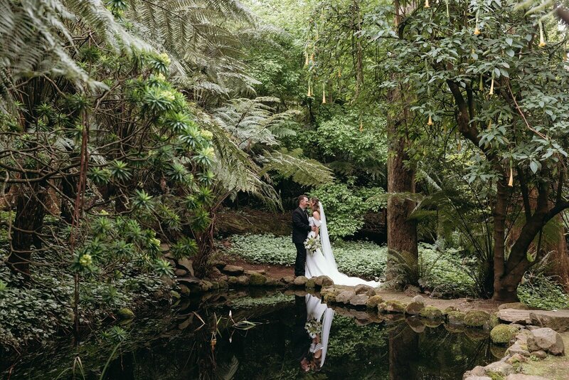 A bride and groom standing next to a pond in lush gardens in the Dandenong Ranges.