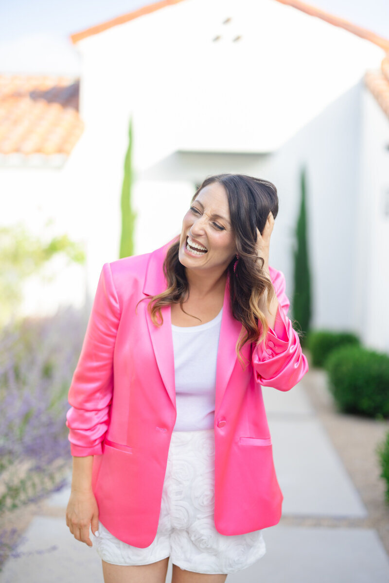 Brand strategist laughing authentically in vibrant pink blazer during outdoor professional photoshoot