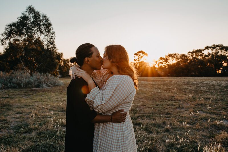 engaged couple sharing a kiss at sunset in the park
