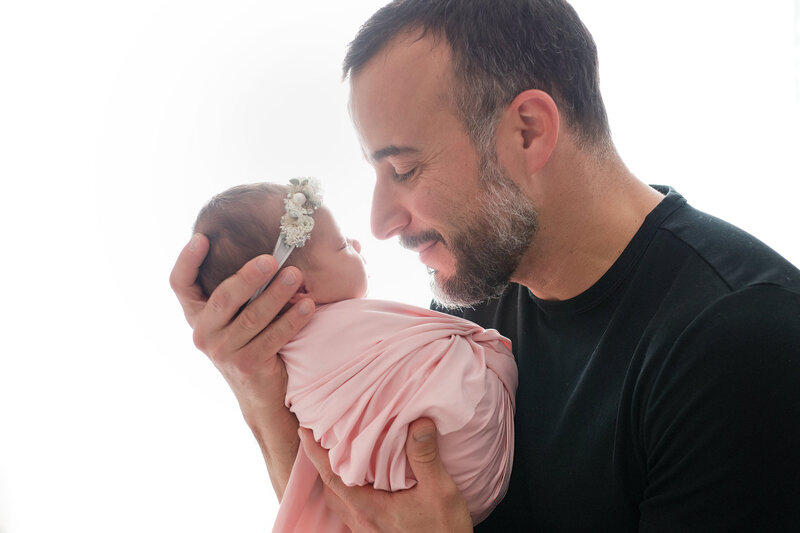 Dad and newborn baby girl nose to nose during photoshoot.