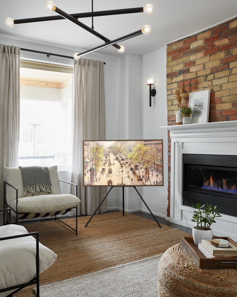 Before and after transformation of a living room into a bright, spacious room with black, white, and earthy tones and featuring a large window, several plush white chairs, a framed painting on a black stand, an elegant white fireplace, modern lighting fixtures, and off-white and beige rugs