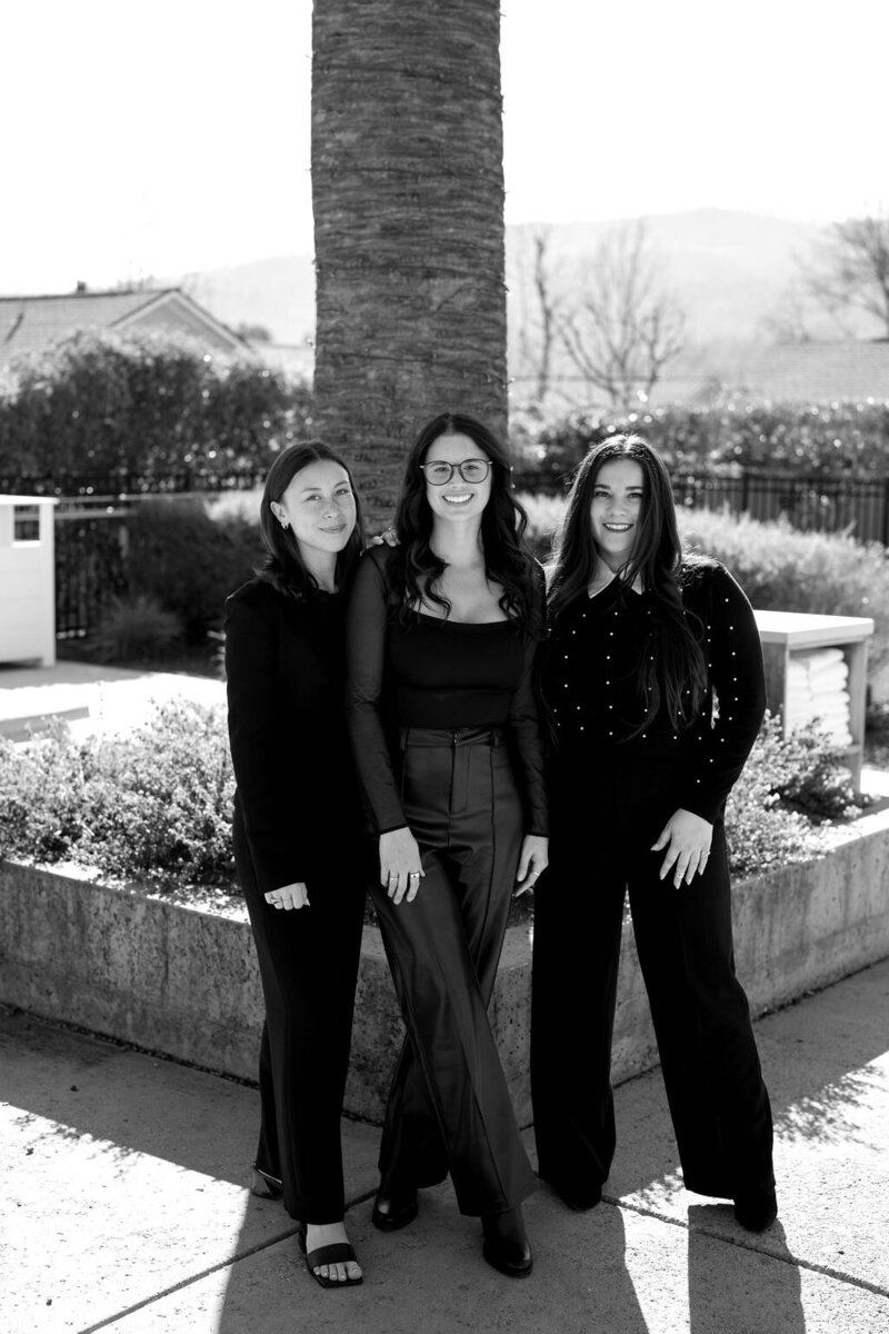 Photography by Logan Alexander. The La Perle Retreats team, including Raquel Bickford, Kristen Chavez, and Claire Glynn, standing together outdoors in elegant black attire.