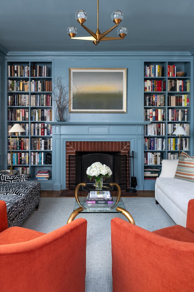Living room with blue walls, built-in bookshelves, a fireplace, a central coffee table, and an orange chair, creating a cozy and elegant space