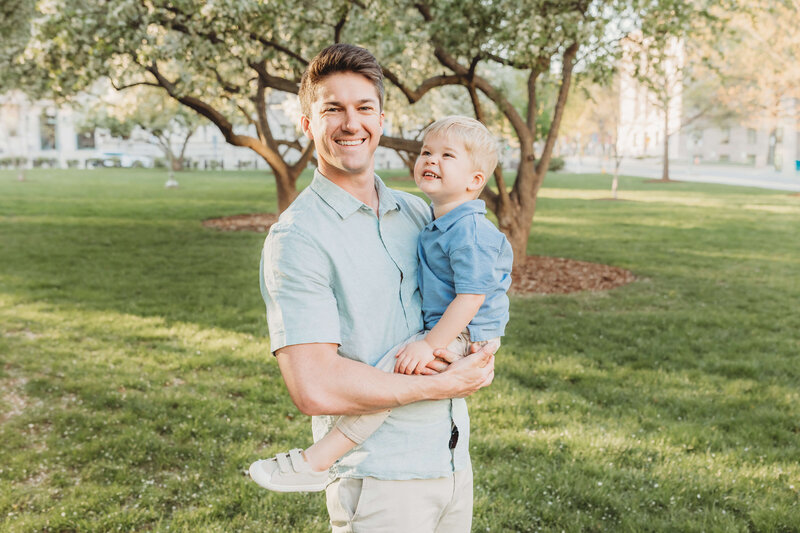 Brown haired dad holding his blonde toddler son as they smile together for a harrisburg family photo 